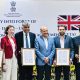 Government officials and industry representatives mark the entry into force of the India–UK CETA while holding framed trade documents.
